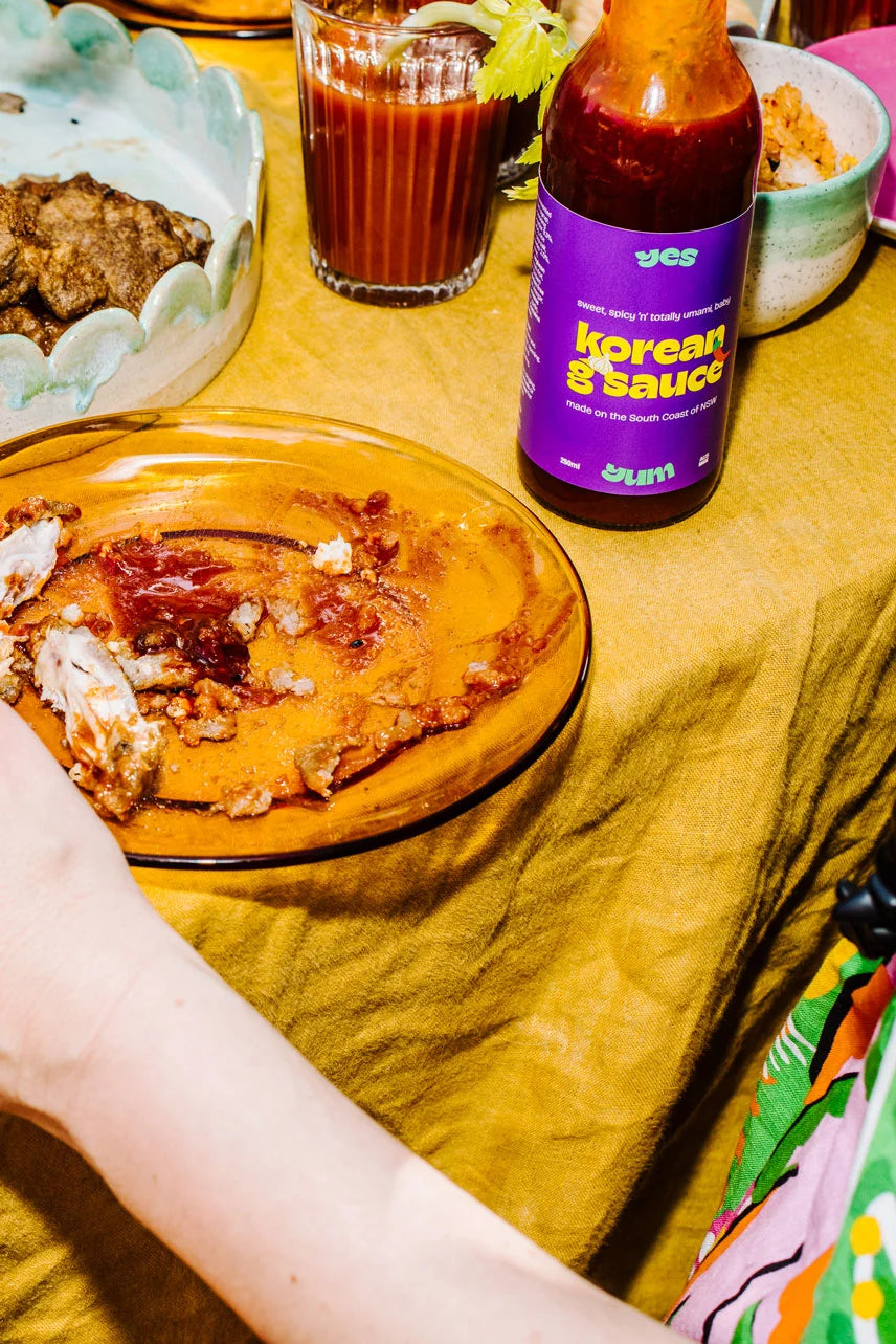 Table with food, drinks, and a bottle of 'Korean Sauce' on a yellow tablecloth.