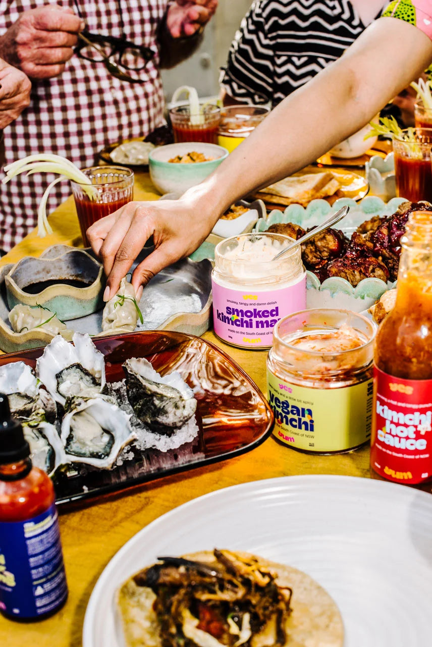 People around a table with food and condiments, including a bottle of Ocean Niche sauce.