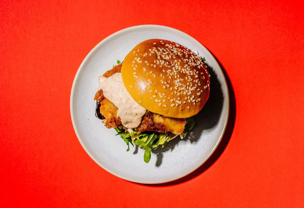Burger with sesame seed bun on a white plate against a red background