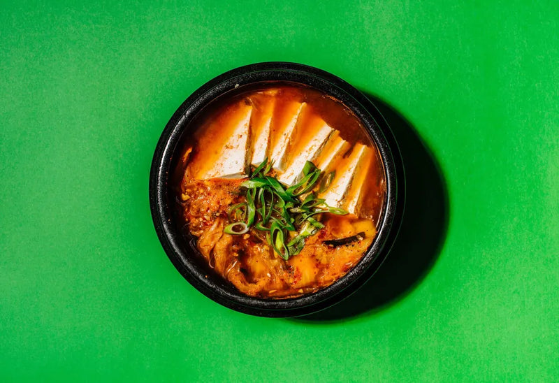 Bowl of soup with noodles and greens on a green background
