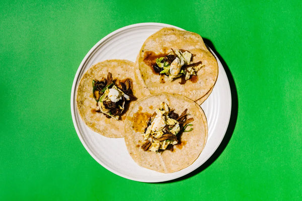 Three tortillas with toppings on a white plate against a green background