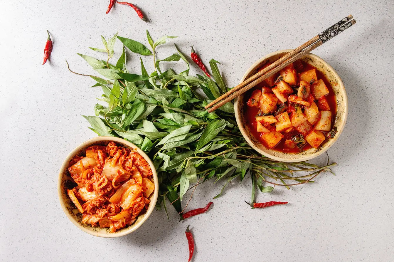 Two bowls of food with green leaves and red peppers on a light gray background
