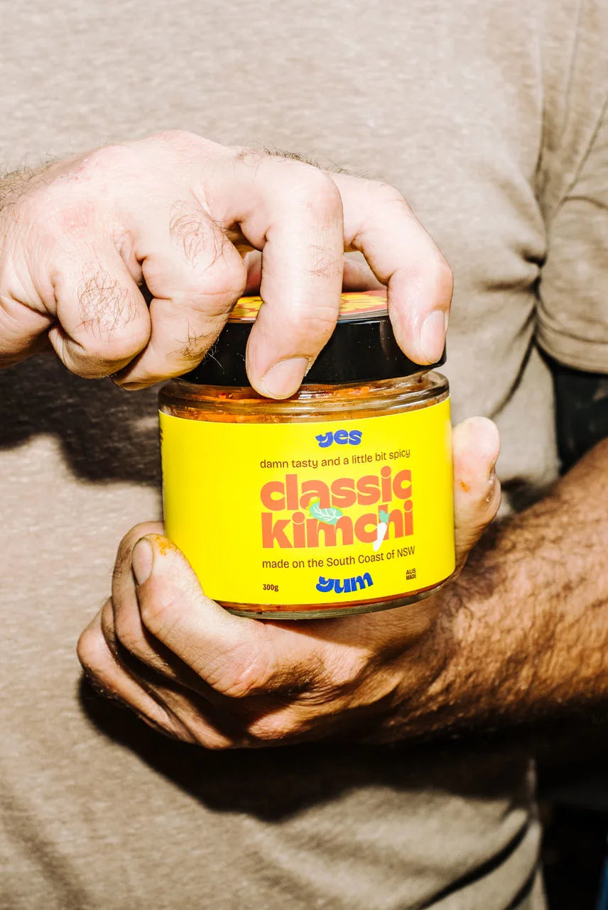 Person opening a jar of 'classic kimchi' with a yellow label.