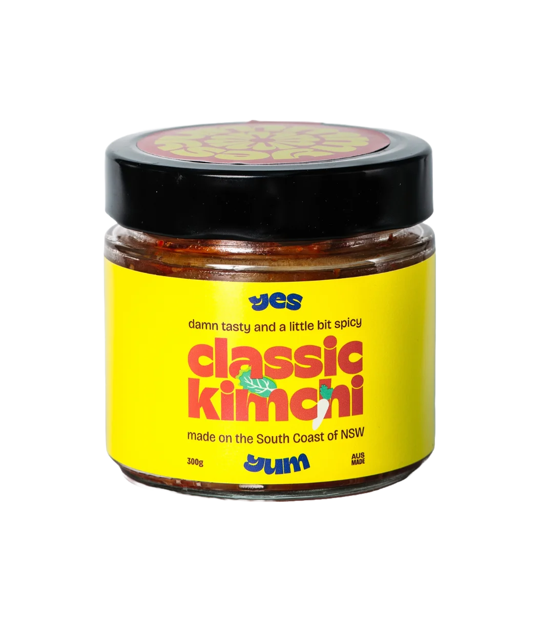 Jar of classic kimchi with yellow label and black lid on a white background