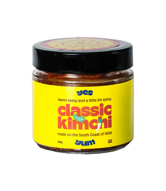 Jar of classic kimchi with yellow label and black lid on a white background