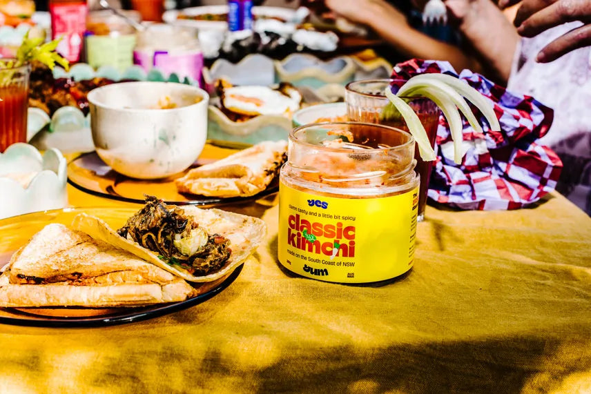 Jar of Kikkoman classic kimchi on a table with food and people in the background