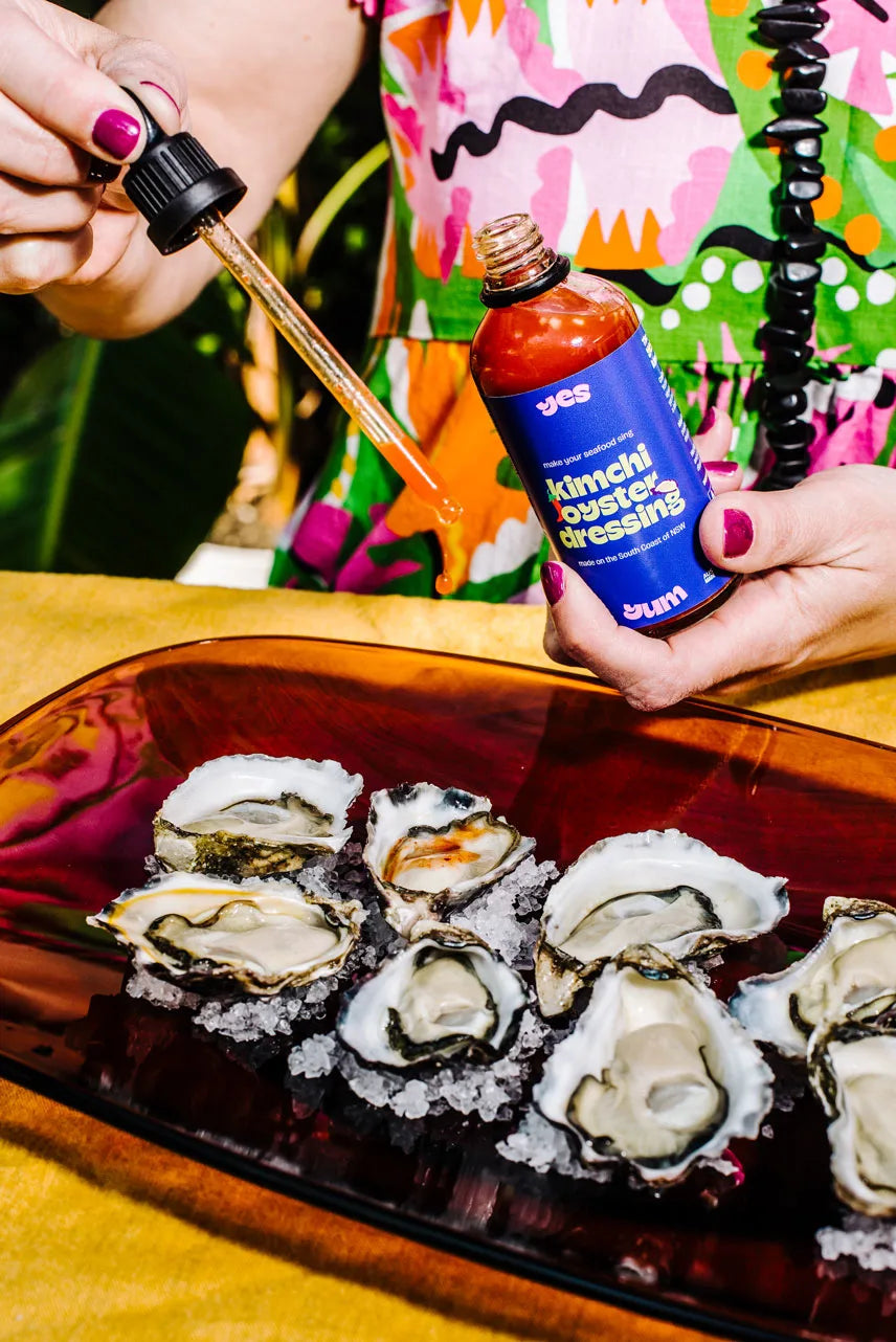 Person holding a bottle of kimchi-oyster-dressing and a dropper over a plate of oysters.