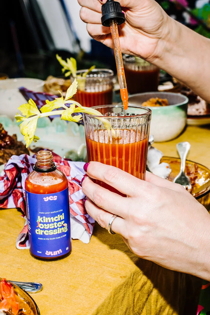Person pouring a red sauce from a bottle into a glass with a colorful background