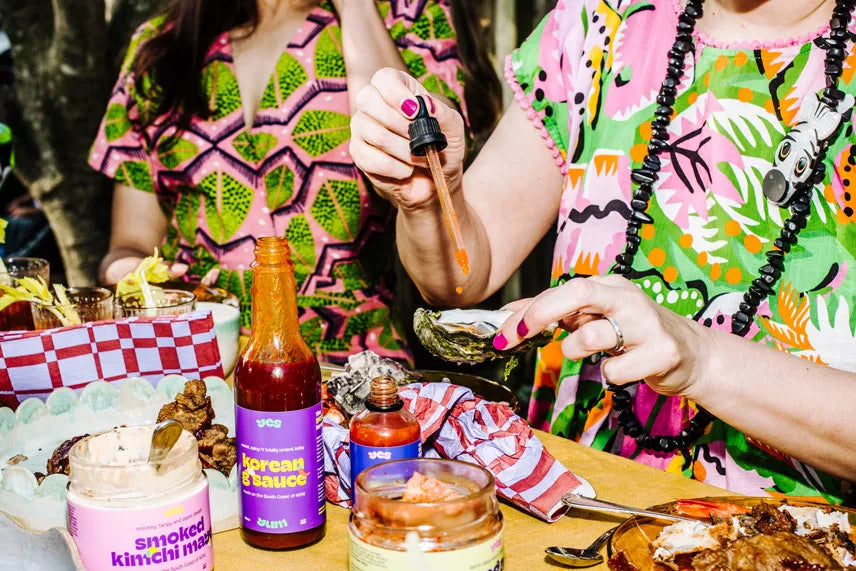 Two people in colorful outfits at a food stall with various condiments and food items.