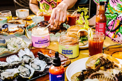 Table with various food items, drinks, and condiments with people partially visible.
