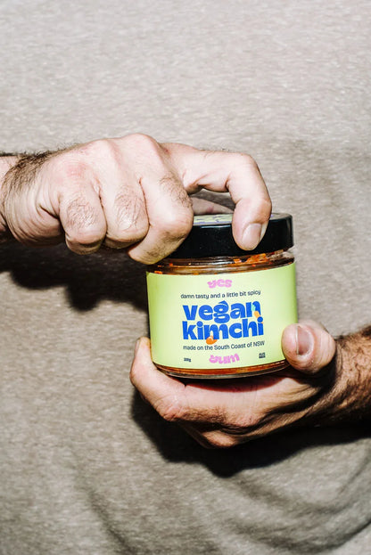 Person holding a jar of vegan kimchi with a green label.